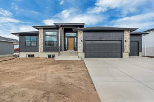 View of front of house with an attached garage, concrete driveway, and stone siding