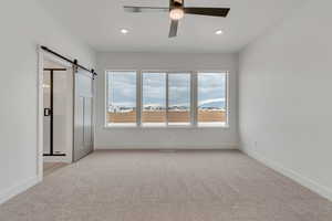Unfurnished bedroom with a barn door, light carpet, and a ceiling fan