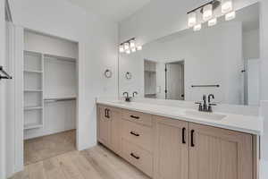 Full bath with double vanity, a walk in closet, and light wood finished floors