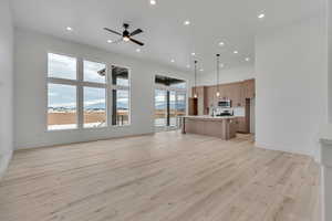 Unfurnished living room featuring a mountain view, recessed lighting, light wood finished floors, a ceiling fan, and a towering ceiling