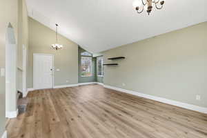 Unfurnished living room featuring a chandelier, high vaulted ceiling, light wood-type flooring, and stairs