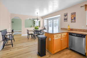 Kitchen with a peninsula, dishwasher, light wood-style flooring, decorative light fixtures, and light countertops