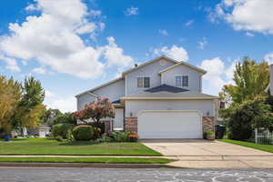 Traditional-style home with a front yard, concrete driveway, brick siding, roof with shingles, and a garage