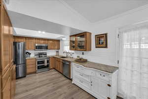 Kitchen with appliances with stainless steel finishes, ornamental molding, decorative backsplash, light stone countertops, and light wood-type flooring