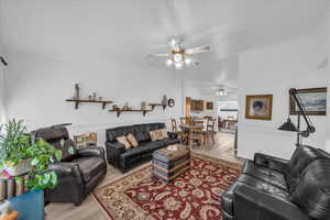 Living room featuring wood finished floors, a ceiling fan, vaulted ceiling, and ornamental molding