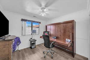 Office area featuring a textured ceiling, light wood-style floors, ceiling fan, and crown molding