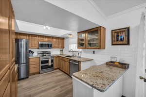 Kitchen with light stone counters, stainless steel appliances, glass insert cabinets, brown cabinetry, and a peninsula