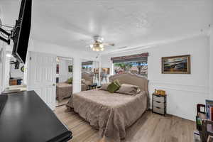 Bedroom with light wood-type flooring, a textured ceiling, ceiling fan, ornamental molding, and two closets