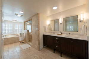 Bathroom with tiled shower, double vanity, a bath, and light tile patterned flooring
