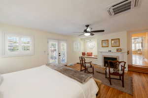 Bedroom featuring access to outside, french doors, wood finished floors, a tile fireplace, and a ceiling fan
