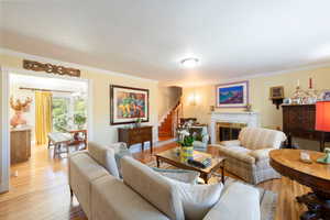 Living room with ornamental molding, a chandelier, a premium fireplace, wood finished floors, and stairs