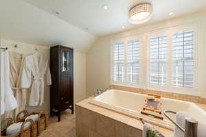 Bathroom featuring a bath, vaulted ceiling, recessed lighting, and light tile patterned floors