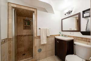 Bathroom with tile walls, vanity, a stall shower, wainscoting, and light tile patterned floors