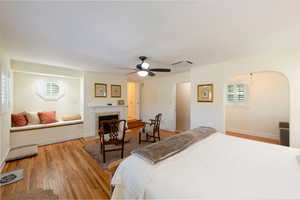 Bedroom with light wood finished floors, arched walkways, ceiling fan, and a fireplace