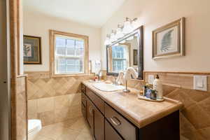 Bathroom with tile walls, wainscoting, vanity, and light tile patterned floors