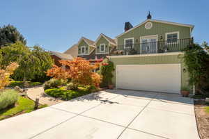View of front of house with driveway, a balcony, an attached garage, and a chimney
