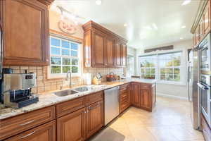 Kitchen featuring decorative backsplash, brown cabinets, light stone counters, appliances with stainless steel finishes, and recessed lighting