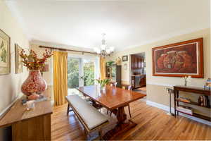 Dining room with light wood-style flooring, a chandelier, ornamental molding, and a wainscoted wall