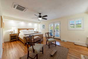 Bedroom featuring cooling unit, access to outside, french doors, light wood-style floors, and a textured ceiling