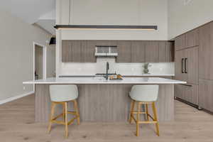 Kitchen with modern cabinets, a kitchen bar, light wood-type flooring, a high ceiling, and an island with sink