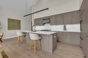 Kitchen with high vaulted ceiling, modern cabinets, a kitchen bar, a center island with sink, and light wood-style floors