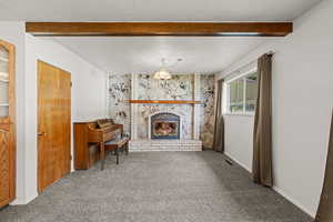 Carpeted living area featuring a textured ceiling, a fireplace, and beam ceiling