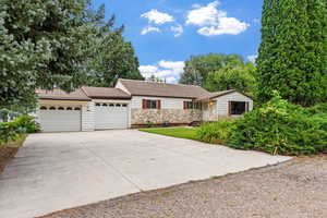Ranch-style home featuring driveway, a garage, a shingled roof, and stone siding