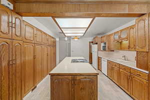 Kitchen featuring light wood-type flooring, light countertops, a center island, and white appliances