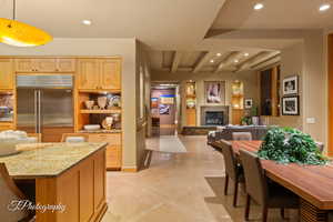 Kitchen featuring beam ceiling, light stone countertops, stainless steel built in refrigerator, recessed lighting, and a stone fireplace