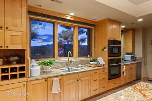 Kitchen with light stone counters, light brown cabinetry, recessed lighting, dishwasher, and light tile patterned floors