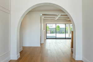 Unfurnished living room with arched walkways, beam ceiling, coffered ceiling, and light wood-type flooring