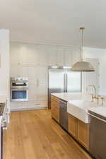 Kitchen featuring high end appliances, pendant lighting, light wood-style flooring, light stone countertops, and light brown cabinets