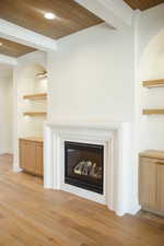 Detailed view of a wooden ceiling with exposed beams, wood finished floors, a glass covered fireplace, and recessed lighting