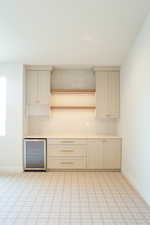 Kitchen with cream cabinets, decorative backsplash, beverage cooler, open shelves, and light floors
