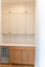 Bar featuring wine cooler, backsplash, and white cabinets
