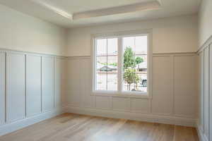 Unfurnished room with a decorative wall, a raised ceiling, light wood-style flooring, and a wainscoted wall