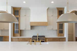 Kitchen with glass insert cabinets, decorative light fixtures, decorative backsplash, recessed lighting, and brown cabinetry