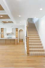 Stairs with beam ceiling, arched walkways, wood finished floors, and recessed lighting