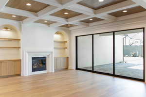 Unfurnished living room with beam ceiling, built in features, a glass covered fireplace, light wood-type flooring, and coffered ceiling