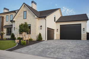 View of front of home with a chimney, stone siding, an attached garage, decorative driveway, and stucco siding