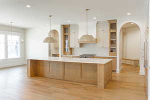 Kitchen featuring arched walkways, glass insert cabinets, backsplash, recessed lighting, and a large island with sink