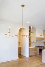 Kitchen featuring a chandelier, tasteful backsplash, high end stove, light wood finished floors, and recessed lighting