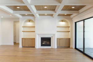Unfurnished living room with beamed ceiling, a fireplace, light wood-style floors, built in shelves, and coffered ceiling