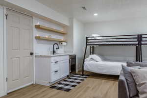Bedroom with a textured ceiling, light wood-style flooring, wine cooler, and recessed lighting