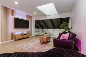 Living room featuring lofted ceiling, a skylight, wood finished floors, and recessed lighting