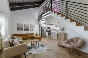 Living area with high vaulted ceiling, light wood finished floors, beam ceiling, and stairway