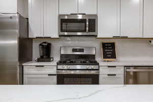 Kitchen featuring stainless steel appliances, decorative backsplash, light stone countertops, and white cabinets