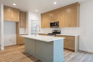 Kitchen with appliances with stainless steel finishes, recessed lighting, light stone counters, light wood-style flooring, and a kitchen island with sink