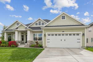 Craftsman-style home with a porch, a front lawn, a shingled roof, driveway, and stone siding