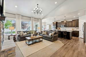 Living area with a chandelier, recessed lighting, a stone fireplace, light wood-type flooring, and high vaulted ceiling